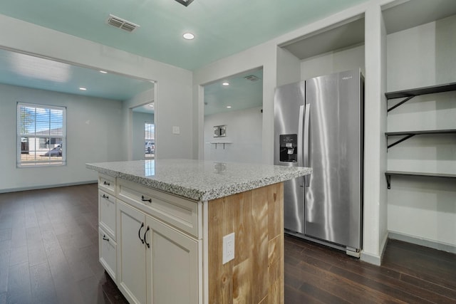 kitchen with white cabinetry, stainless steel fridge, a center island, light stone countertops, and dark wood-type flooring