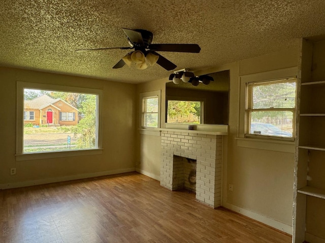 unfurnished living room with ceiling fan, a textured ceiling, a brick fireplace, and light hardwood / wood-style flooring