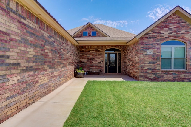 4902 Marshall St, Lubbock, TX 79416 - view of exterior entry with brick siding, a lawn, a shingled roof, and a patio