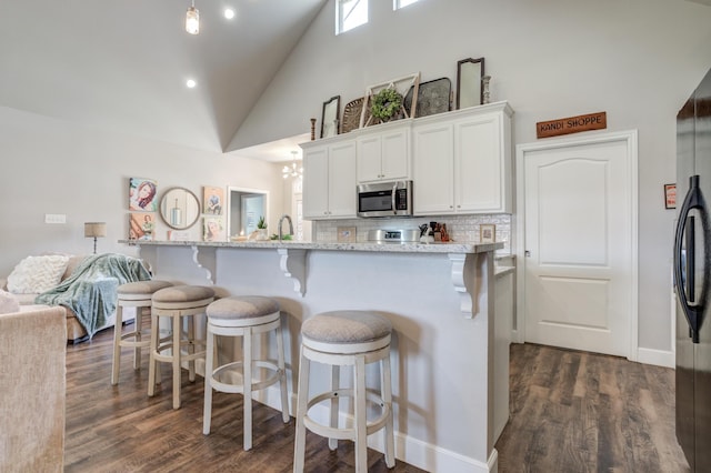 4902 Marshall St, Lubbock, TX 79416 - kitchen featuring stainless steel microwave, high vaulted ceiling, white cabinetry, decorative backsplash, and a breakfast bar