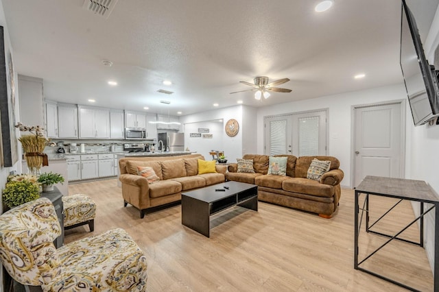 living room featuring french doors, ceiling fan, light hardwood / wood-style flooring, and a textured ceiling