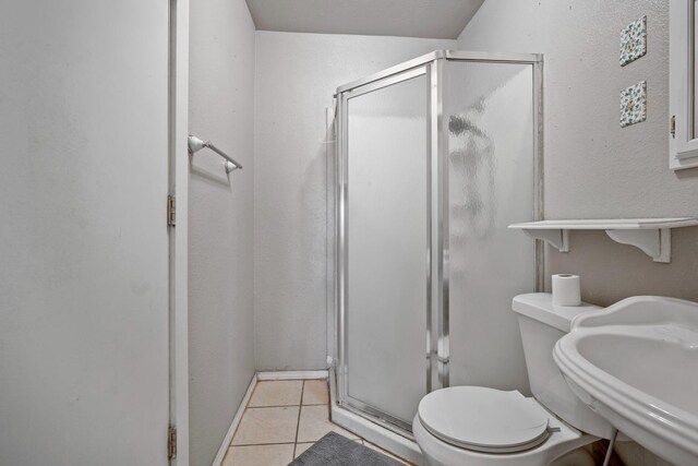 bathroom with an enclosed shower, sink, tile patterned floors, and toilet