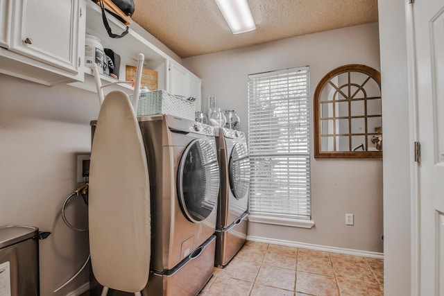 laundry room with a textured ceiling, light tile patterned flooring, washing machine and dryer, baseboards, and cabinet space