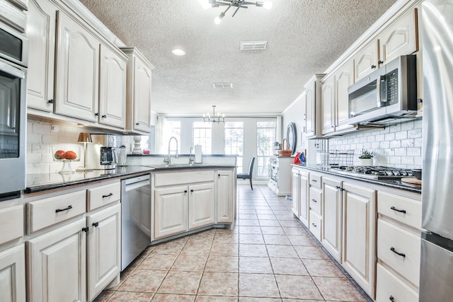 kitchen featuring light tile patterned floors, dark countertops, visible vents, appliances with stainless steel finishes, and a sink