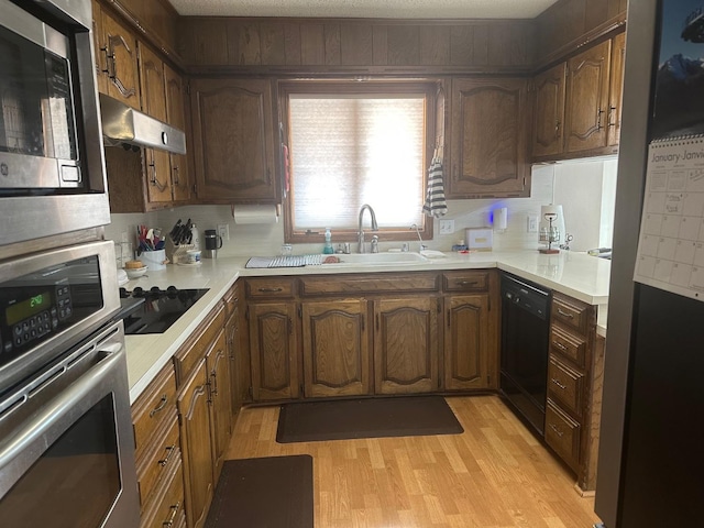 kitchen featuring a textured ceiling, sink, light hardwood / wood-style flooring, and black appliances