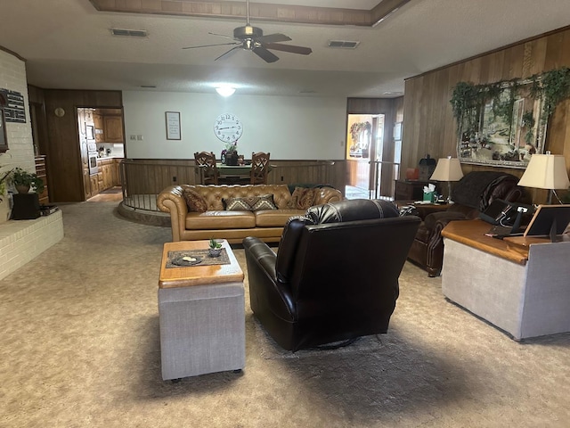 living room with light carpet, a raised ceiling, ceiling fan, and wood walls