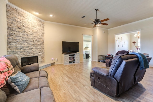 living room with crown molding, a stone fireplace, ceiling fan with notable chandelier, and light hardwood / wood-style flooring