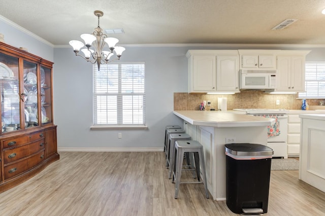 kitchen with white cabinets, decorative light fixtures, light hardwood / wood-style floors, and stove