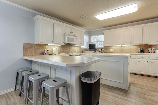 kitchen with tasteful backsplash, white cabinetry, a kitchen bar, and kitchen peninsula