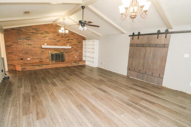 unfurnished living room featuring wood-type flooring, a barn door, lofted ceiling with beams, and a brick fireplace