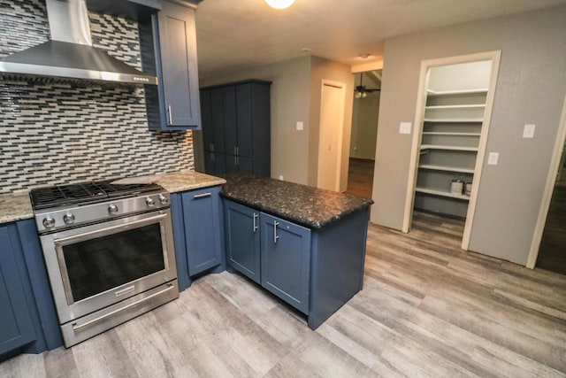 kitchen featuring blue cabinets, gas range, and wall chimney range hood