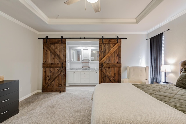 bedroom featuring a barn door, a raised ceiling, ensuite bath, and crown molding