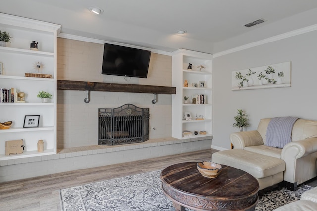 living area featuring visible vents, wood finished floors, ornamental molding, and a brick fireplace