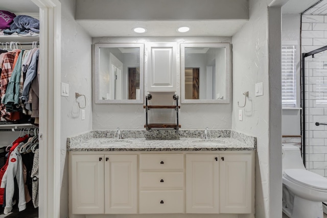 full bath featuring double vanity, toilet, a textured wall, and a sink