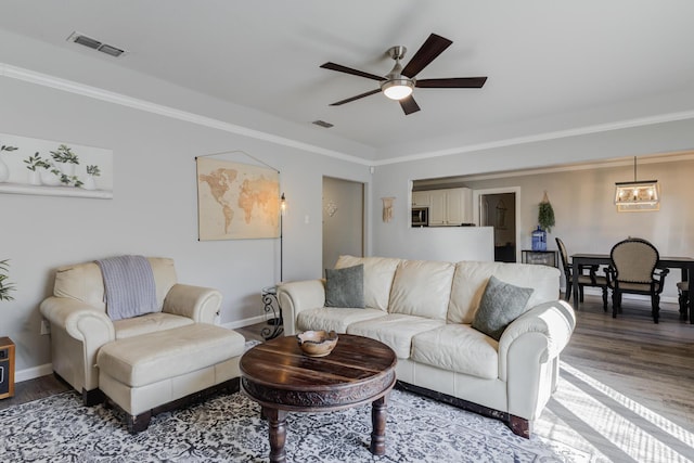 living room featuring baseboards, visible vents, wood finished floors, and ceiling fan with notable chandelier