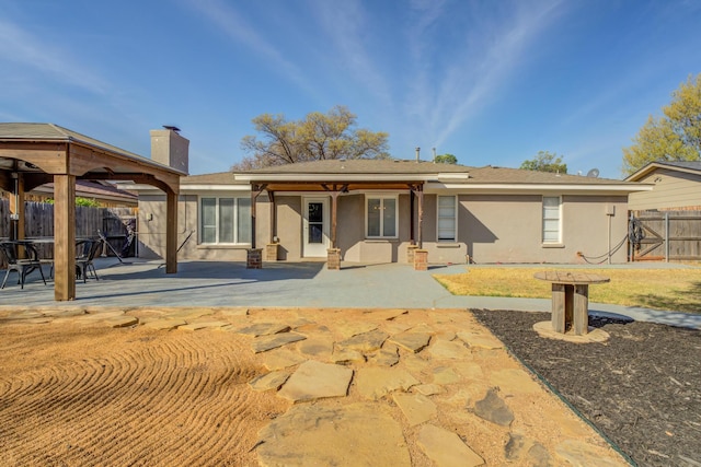 rear view of house with a gazebo, fence, stucco siding, and a patio area
