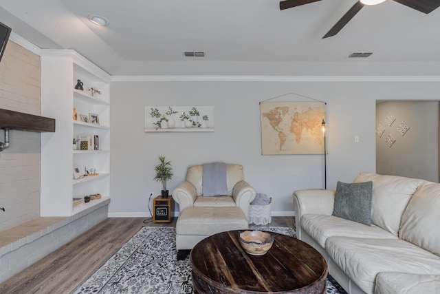 living room with wood finished floors, ceiling fan, built in shelves, baseboards, and visible vents