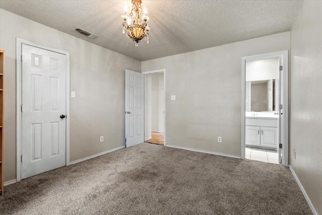 unfurnished bedroom with light carpet, a chandelier, a textured ceiling, and ensuite bathroom