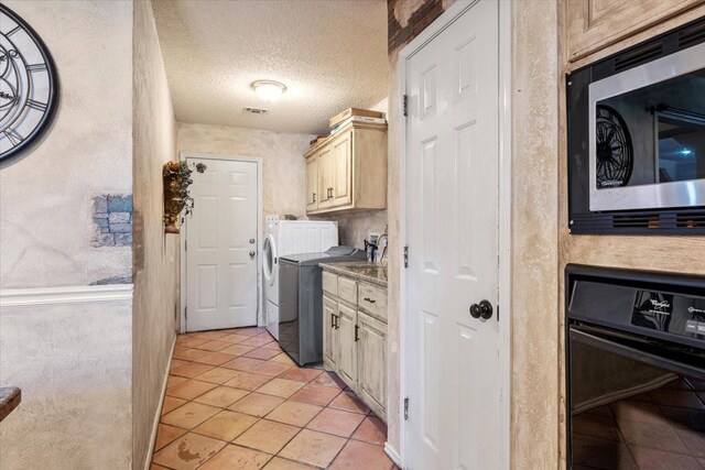 kitchen with stainless steel microwave, black oven, light tile patterned floors, washing machine and dryer, and a textured ceiling