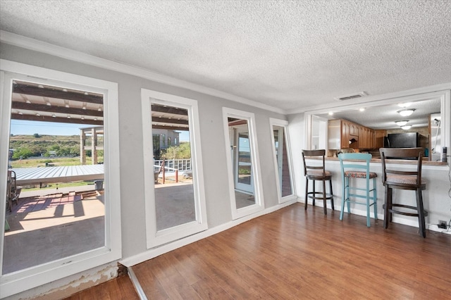 kitchen featuring refrigerator, hardwood / wood-style floors, ornamental molding, a textured ceiling, and a kitchen bar