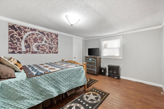 bedroom with hardwood / wood-style flooring, crown molding, a wood stove, and a textured ceiling