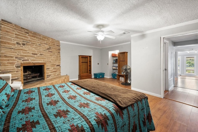 bedroom with crown molding, hardwood / wood-style flooring, ceiling fan, a textured ceiling, and a stone fireplace