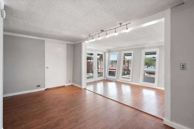 empty room featuring french doors, a textured ceiling, track lighting, ornamental molding, and hardwood / wood-style flooring