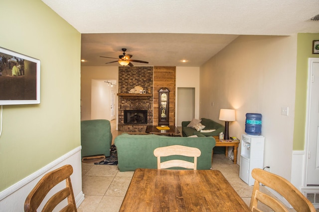 dining space with a ceiling fan, light tile patterned flooring, wainscoting, and a fireplace