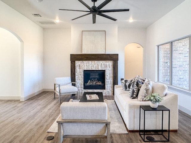 living room with hardwood / wood-style flooring, ceiling fan, and a stone fireplace