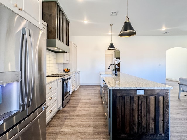 kitchen with hardwood / wood-style flooring, a kitchen island with sink, stainless steel appliances, white cabinets, and decorative light fixtures