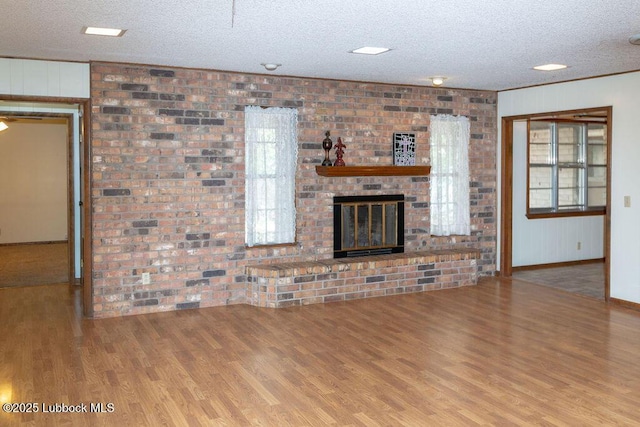 303 Comanche Trl, Tulia, TX 79088 - unfurnished living room featuring wood finished floors, a textured ceiling, brick wall, and a fireplace