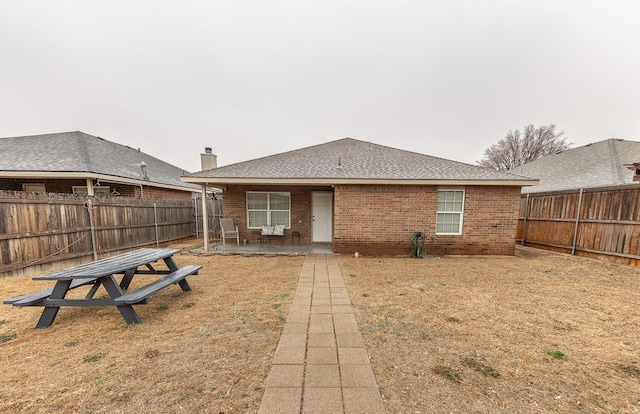 rear view of house with a patio, brick siding, a chimney, and a fenced backyard