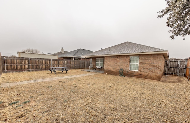 back of house featuring brick siding, a fenced backyard, and roof with shingles