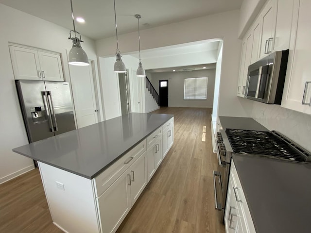 kitchen with white cabinetry, decorative light fixtures, light wood-type flooring, a kitchen island, and stainless steel appliances