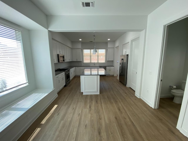 kitchen with a center island, premium appliances, pendant lighting, light hardwood / wood-style floors, and white cabinets