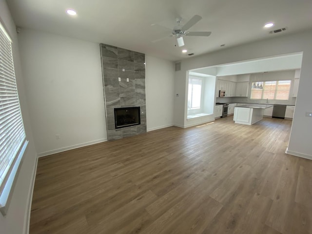 unfurnished living room with sink, hardwood / wood-style flooring, a tile fireplace, and ceiling fan