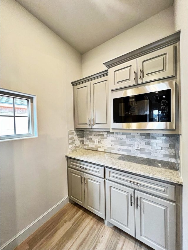 interior space featuring built in microwave, light stone countertops, light hardwood / wood-style floors, and decorative backsplash