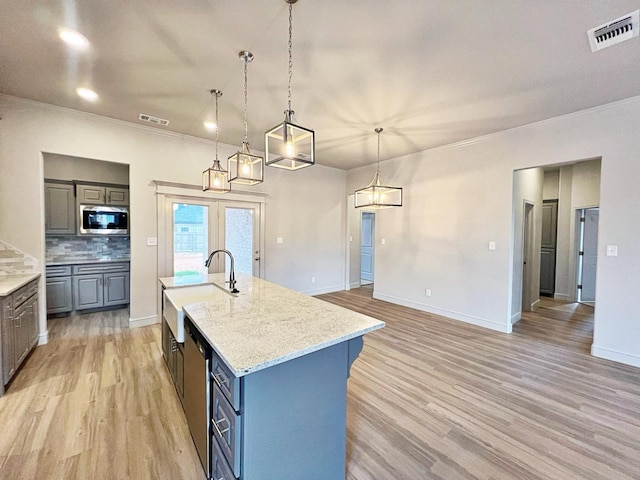 kitchen with light stone counters, decorative light fixtures, light hardwood / wood-style flooring, stainless steel microwave, and an island with sink