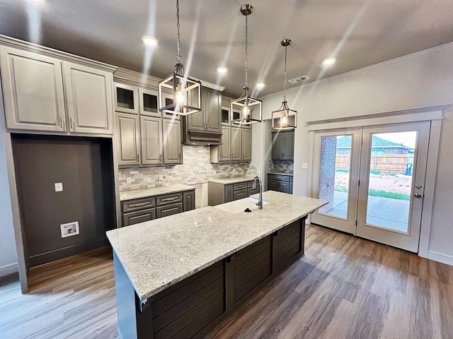 kitchen featuring sink, hanging light fixtures, light stone countertops, an island with sink, and decorative backsplash