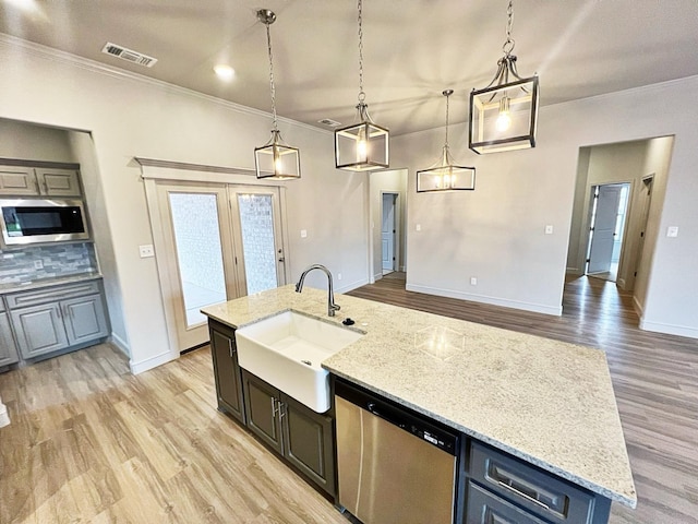 kitchen featuring appliances with stainless steel finishes, sink, hanging light fixtures, a kitchen island with sink, and light stone countertops