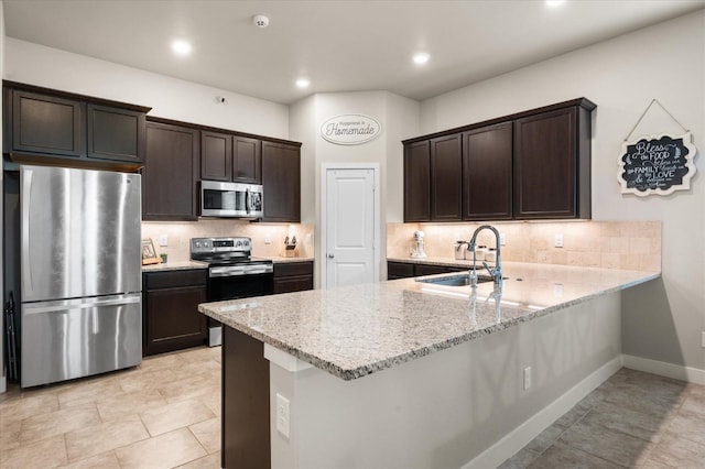 kitchen with sink, appliances with stainless steel finishes, dark brown cabinets, light stone counters, and kitchen peninsula