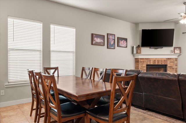 tiled dining space with a brick fireplace and ceiling fan