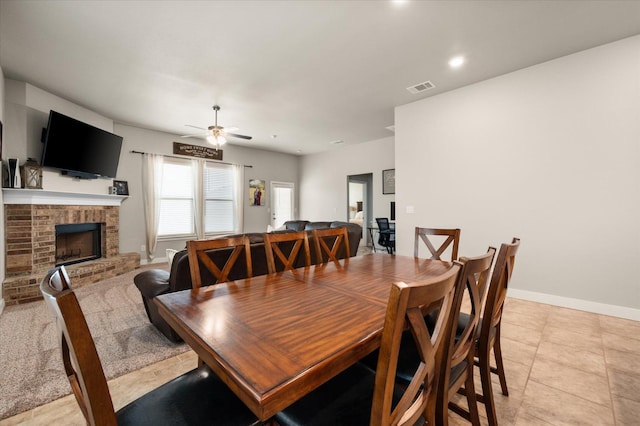 tiled dining area featuring ceiling fan and a fireplace