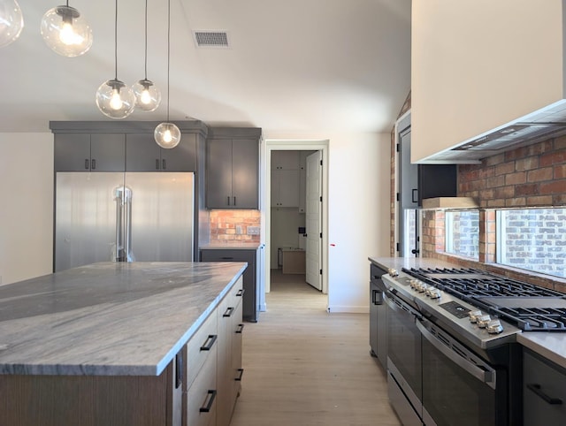 kitchen featuring appliances with stainless steel finishes, pendant lighting, backsplash, wall chimney range hood, and light hardwood / wood-style flooring