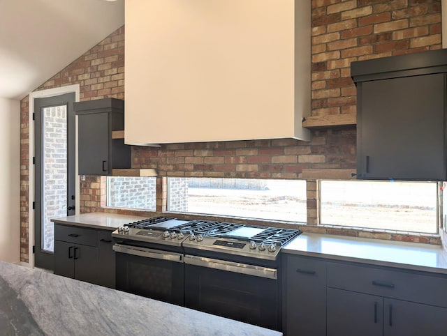 kitchen featuring gray cabinets, lofted ceiling, backsplash, and stainless steel gas stove