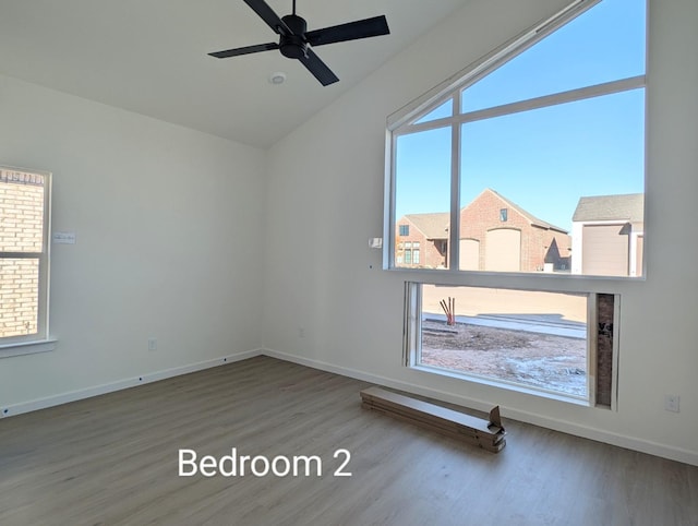 spare room featuring lofted ceiling, ceiling fan, hardwood / wood-style flooring, and a healthy amount of sunlight