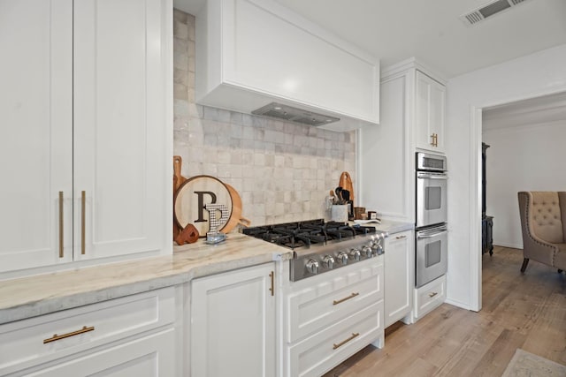 kitchen featuring white cabinetry, backsplash, stainless steel appliances, light stone countertops, and light wood-type flooring