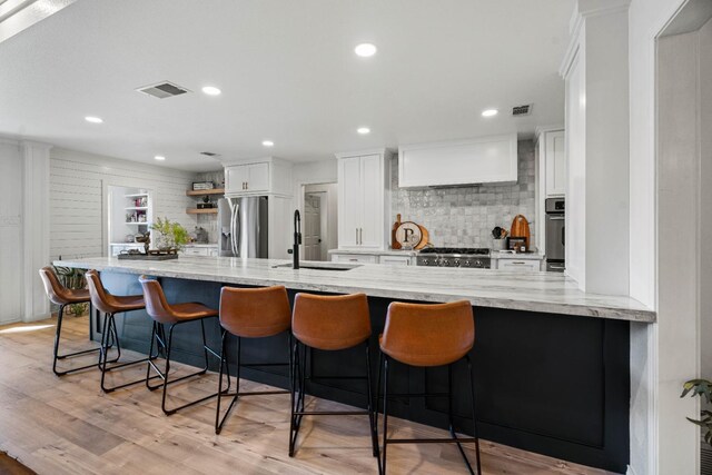 kitchen featuring sink, light stone counters, appliances with stainless steel finishes, a kitchen breakfast bar, and white cabinets