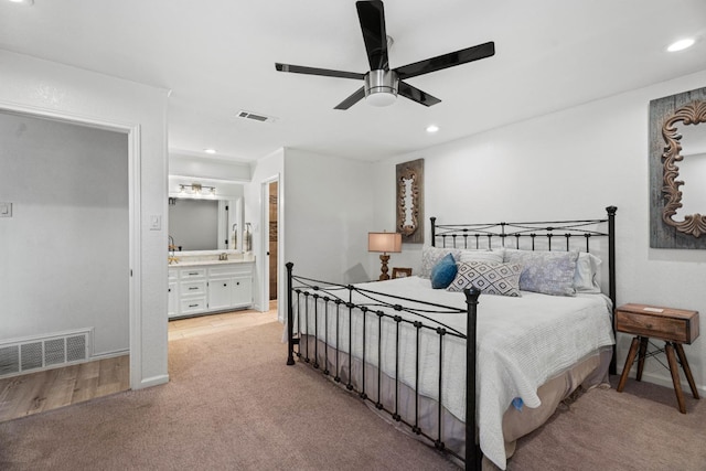 bedroom featuring ceiling fan, light colored carpet, and ensuite bath