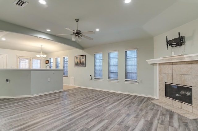 unfurnished living room featuring lofted ceiling, ceiling fan with notable chandelier, a fireplace, and light hardwood / wood-style floors